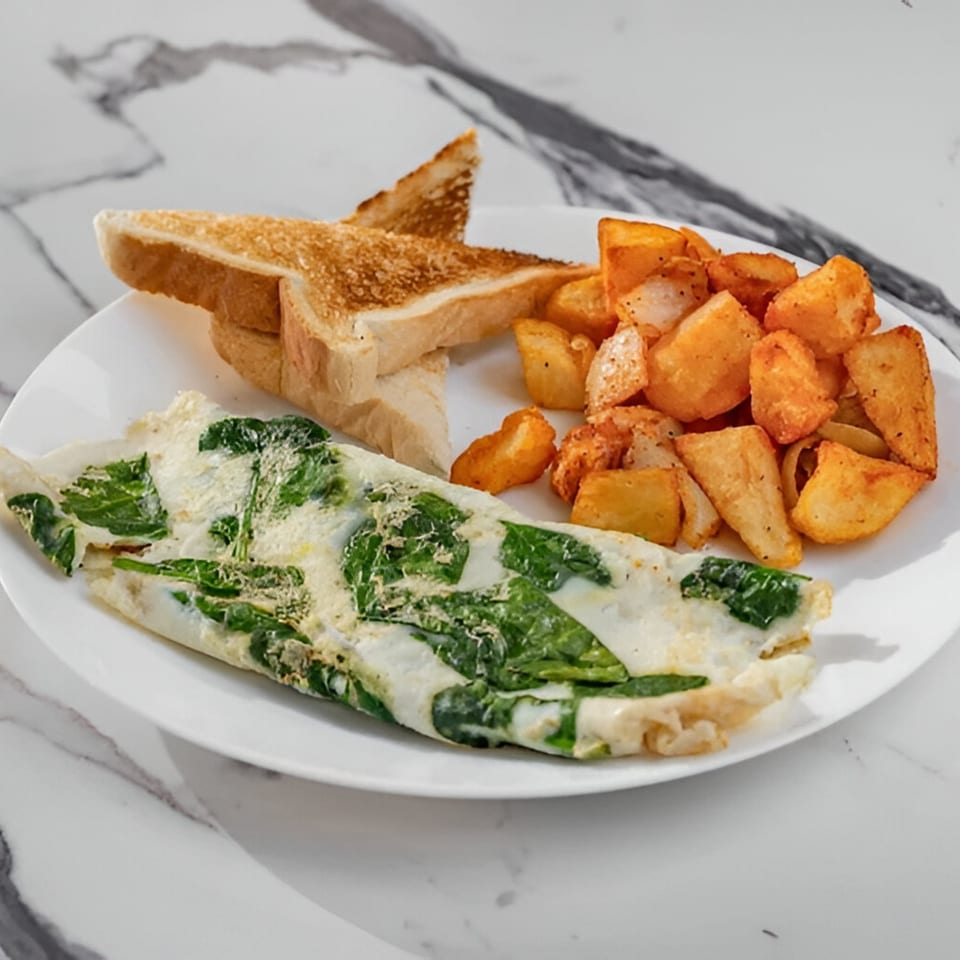 A Delicious Bagels spinach omelet with home fries and toast on a white plate.